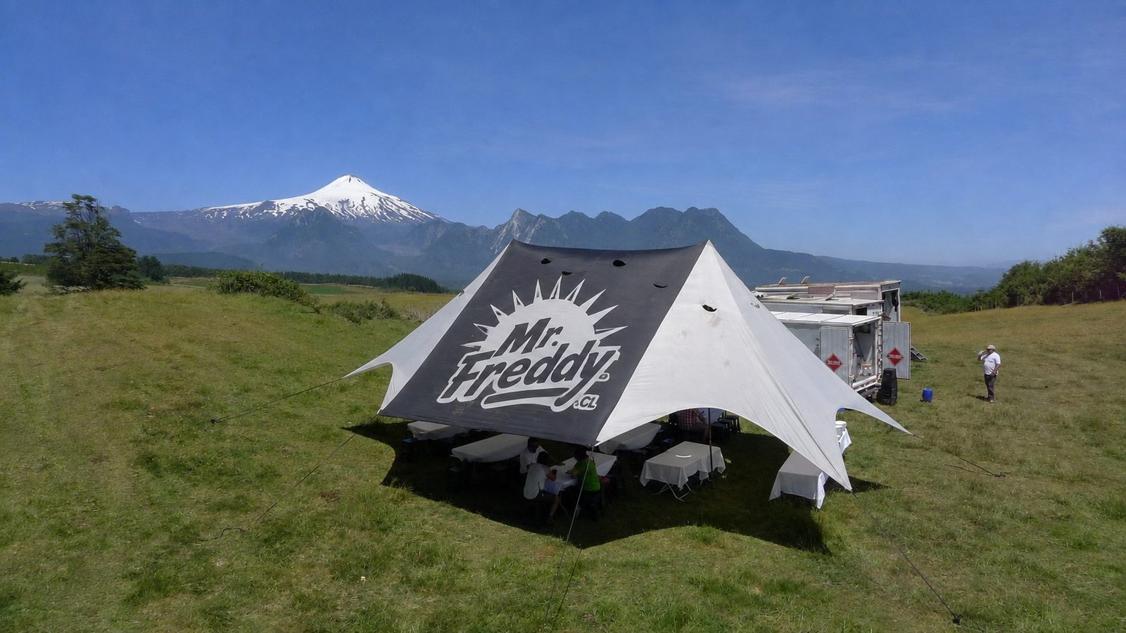 Toldo y camión-cocina MR FREDDY montados en pradera, con volcán nevado al fondo